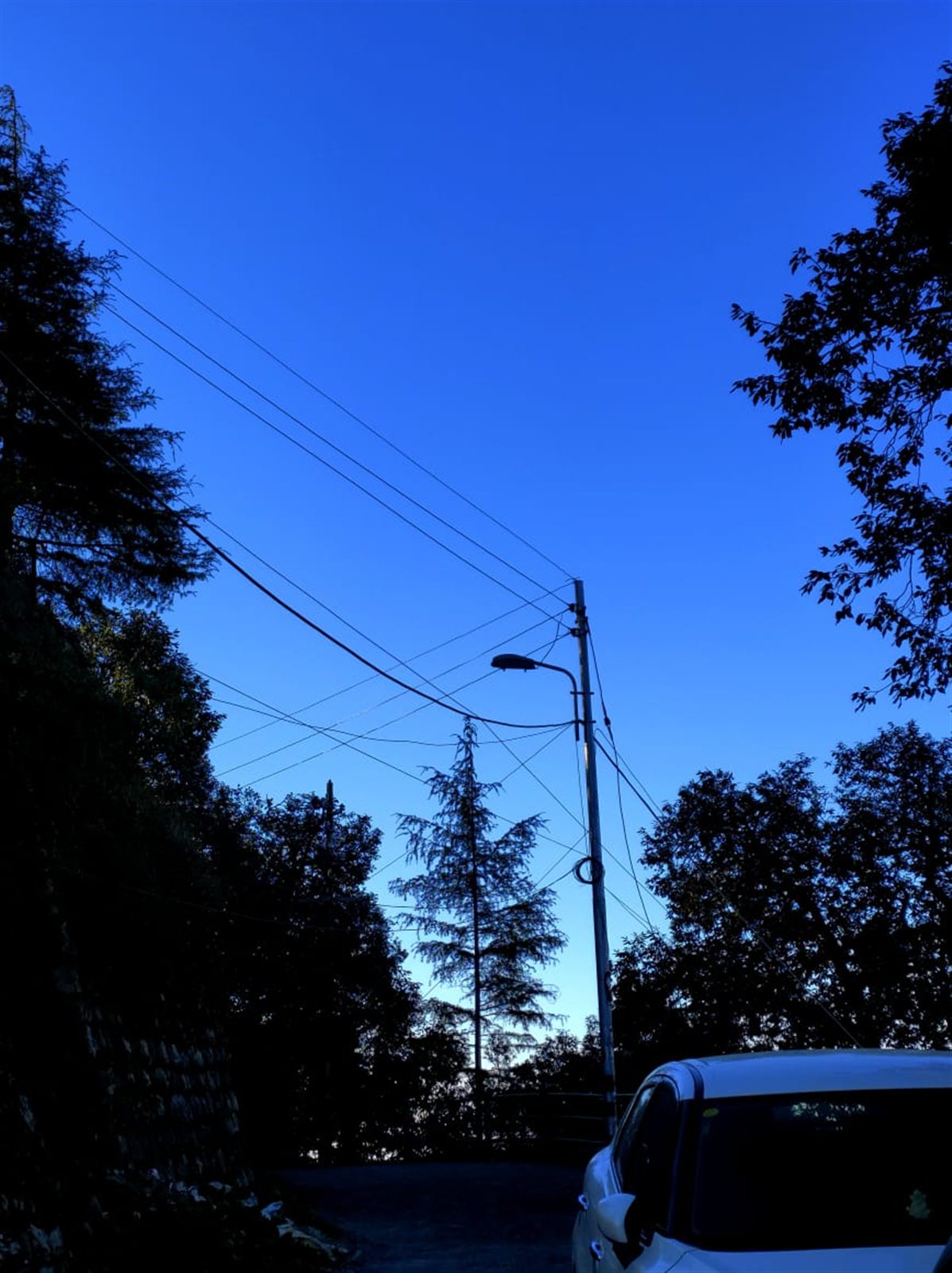 Power lines and a parked car against a deep blue evening sky.