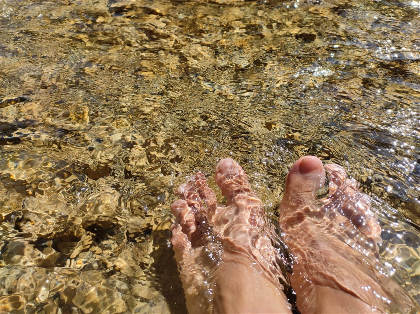 Feet resting in a clear, shallow mountain stream.
